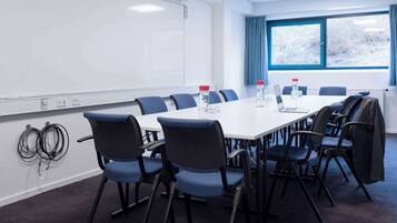 A conference room with a whiteboard, a long table with chairs, and a window with blue curtains.