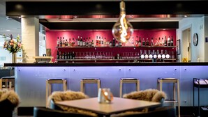A bar area with a red back wall, multiple shelves of liquor bottles, and a row of bar stools. - Scandic Odense (Odense)