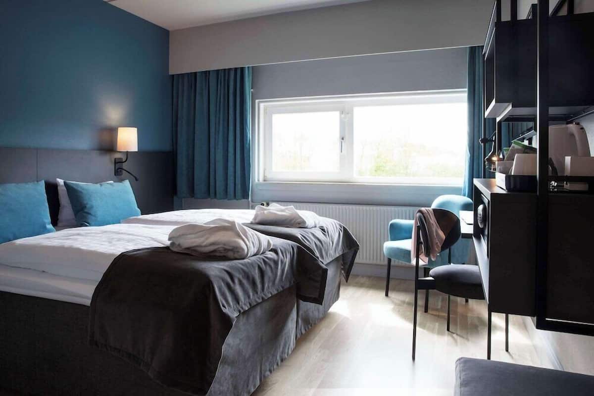 Una habitación de hotel moderna con una cama grande, un escritorio y una ventana con cortinas.