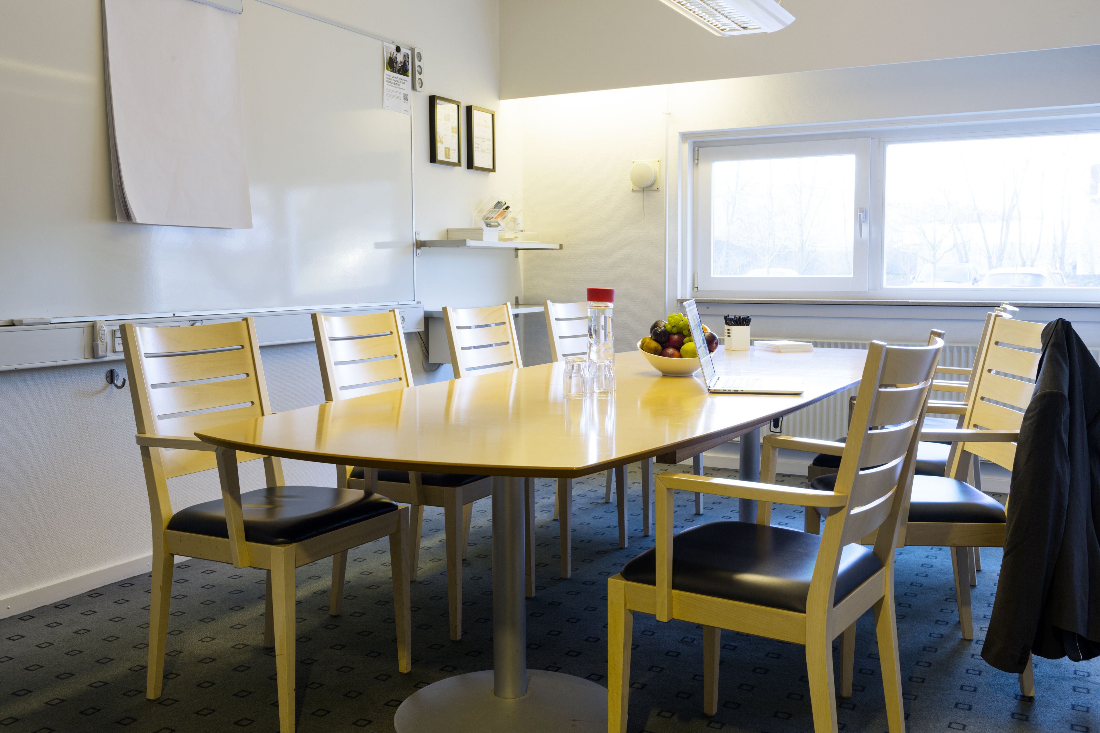 Una sala de conferències amb una taula gran, cadires, una pissarra i una finestra amb vistes.