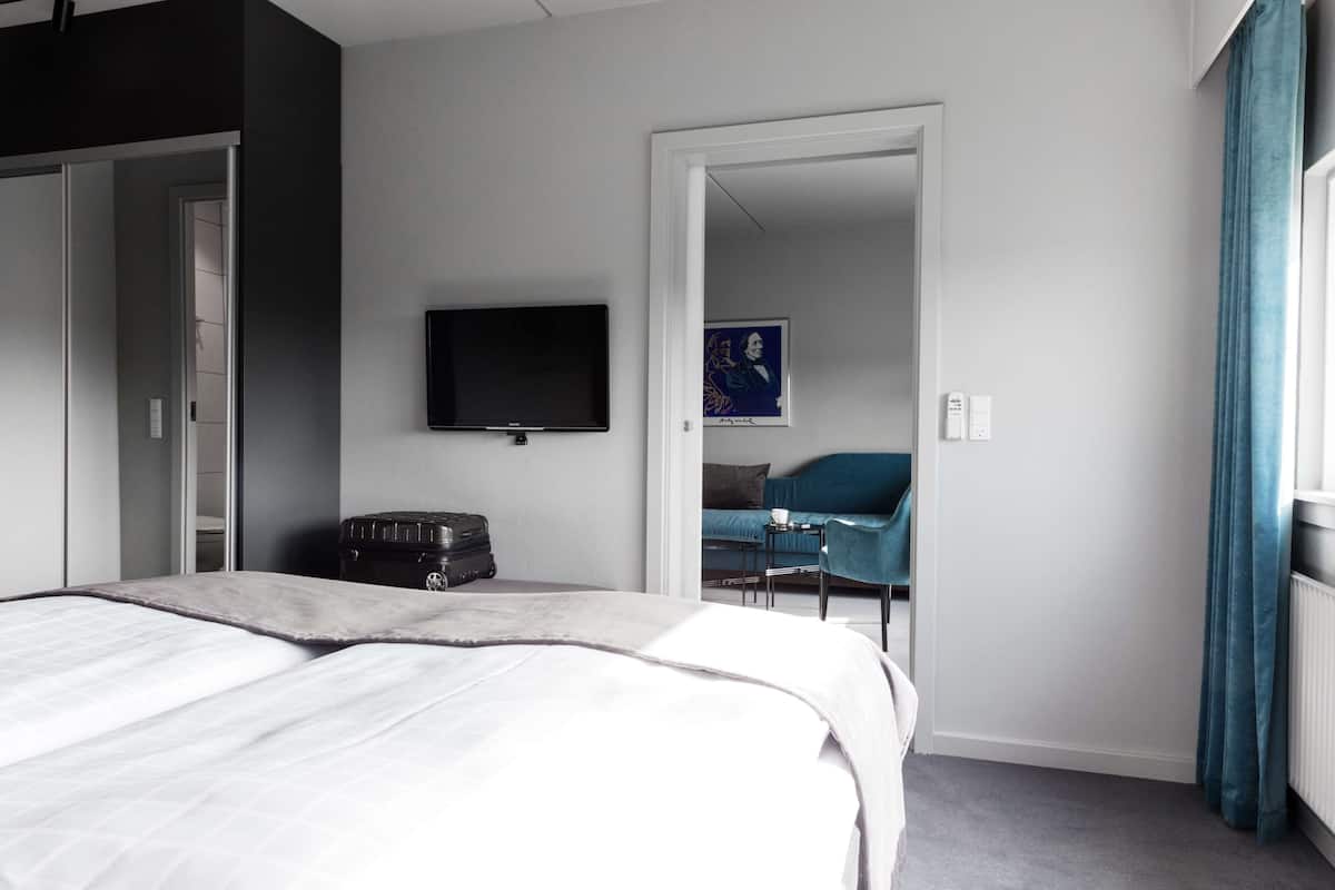 Habitación de hotel con una cama, un escritorio con silla, un televisor y una obra de arte azul en la pared.