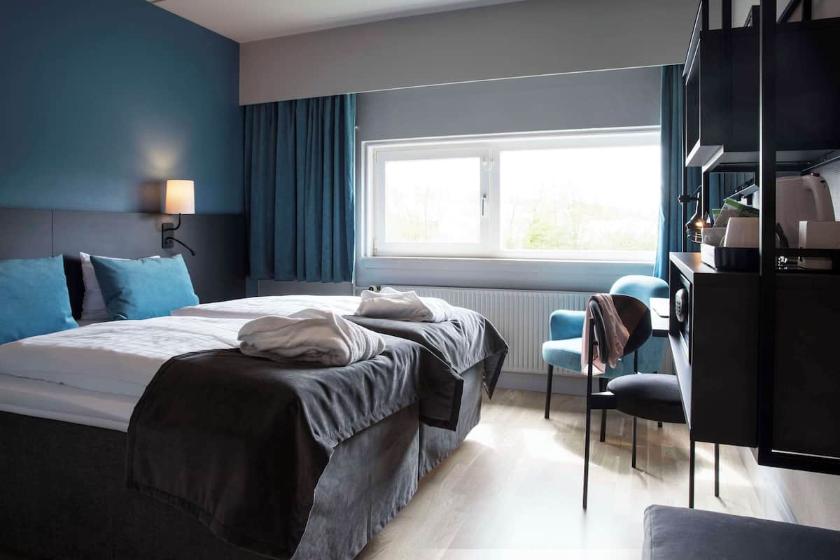 Una habitación de hotel moderna con una cama grande, un escritorio y una ventana con cortinas.