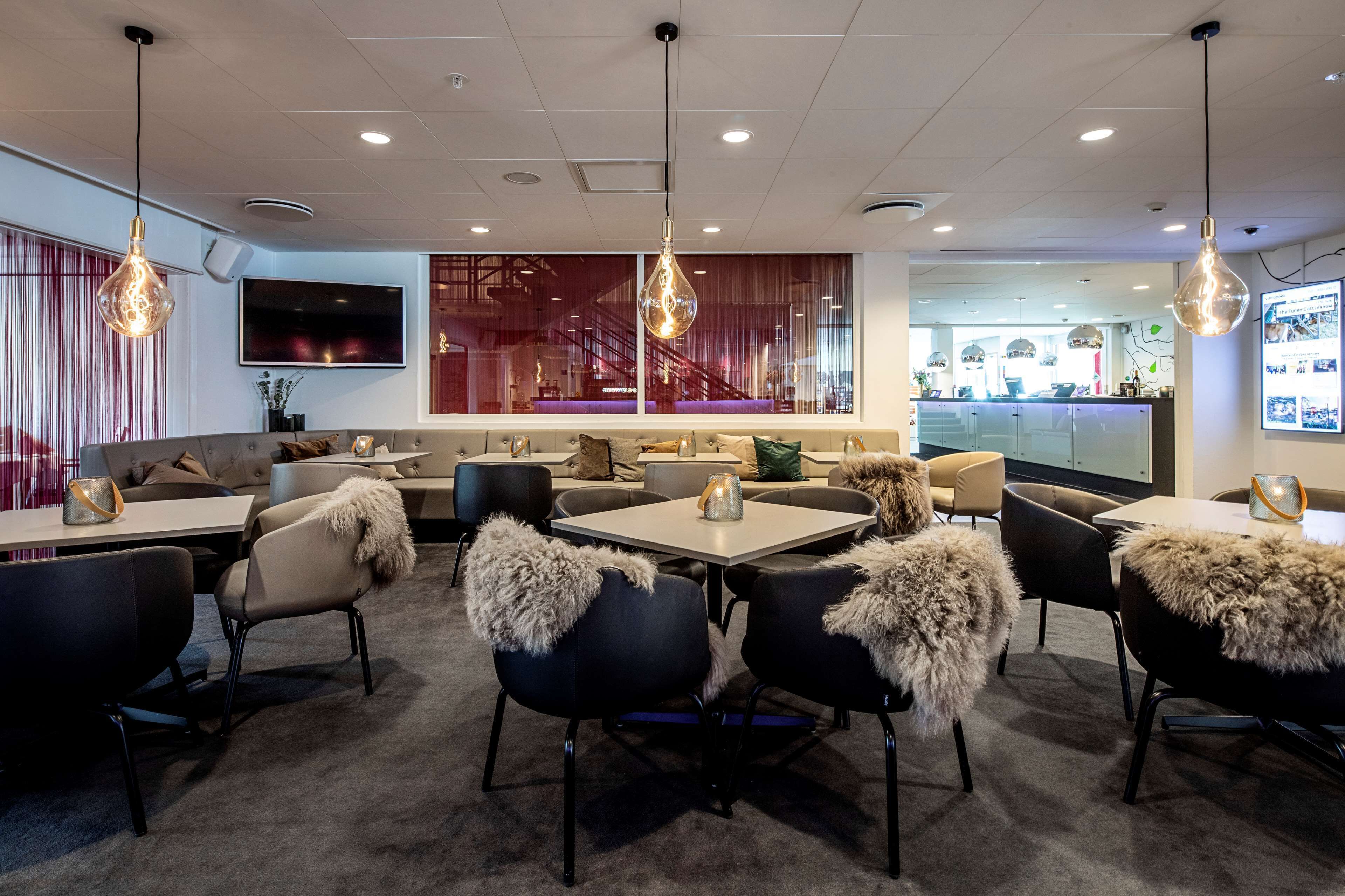 A modern dining area with tables and chairs, a bar in the background, and a large TV on the wall.