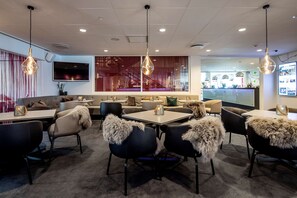 A modern dining area with tables and chairs, a bar in the background, and a large TV on the wall. - Scandic Odense (Odense)
