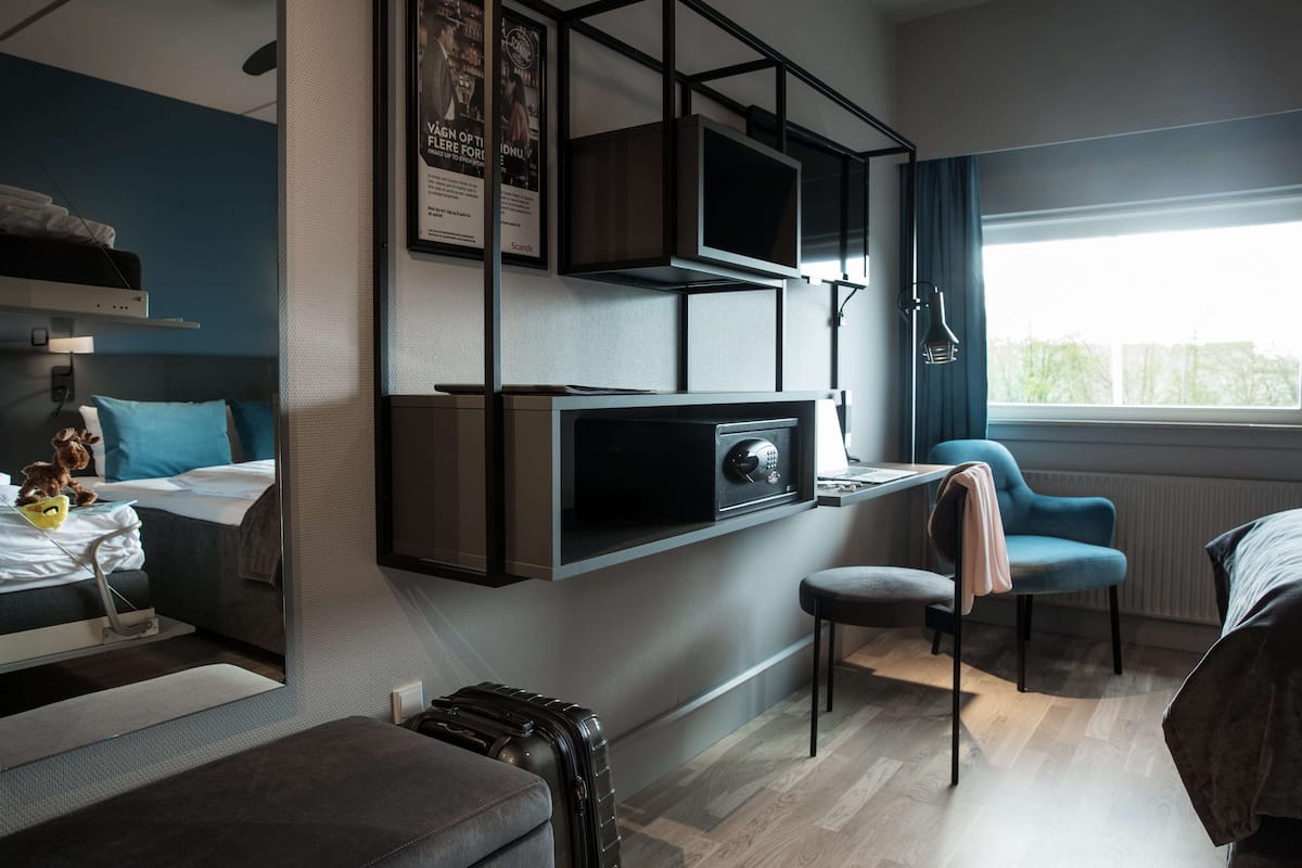 Habitación de hotel moderna con cama, escritorio, silla, maleta y ventana con vistas.