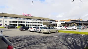 Un parcheggio con diverse auto parcheggiate di fronte a un edificio con la scritta 'Scandic'.