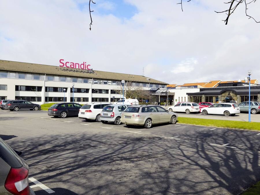 Un parcheggio con diverse auto parcheggiate di fronte a un edificio con la scritta 'Scandic'.