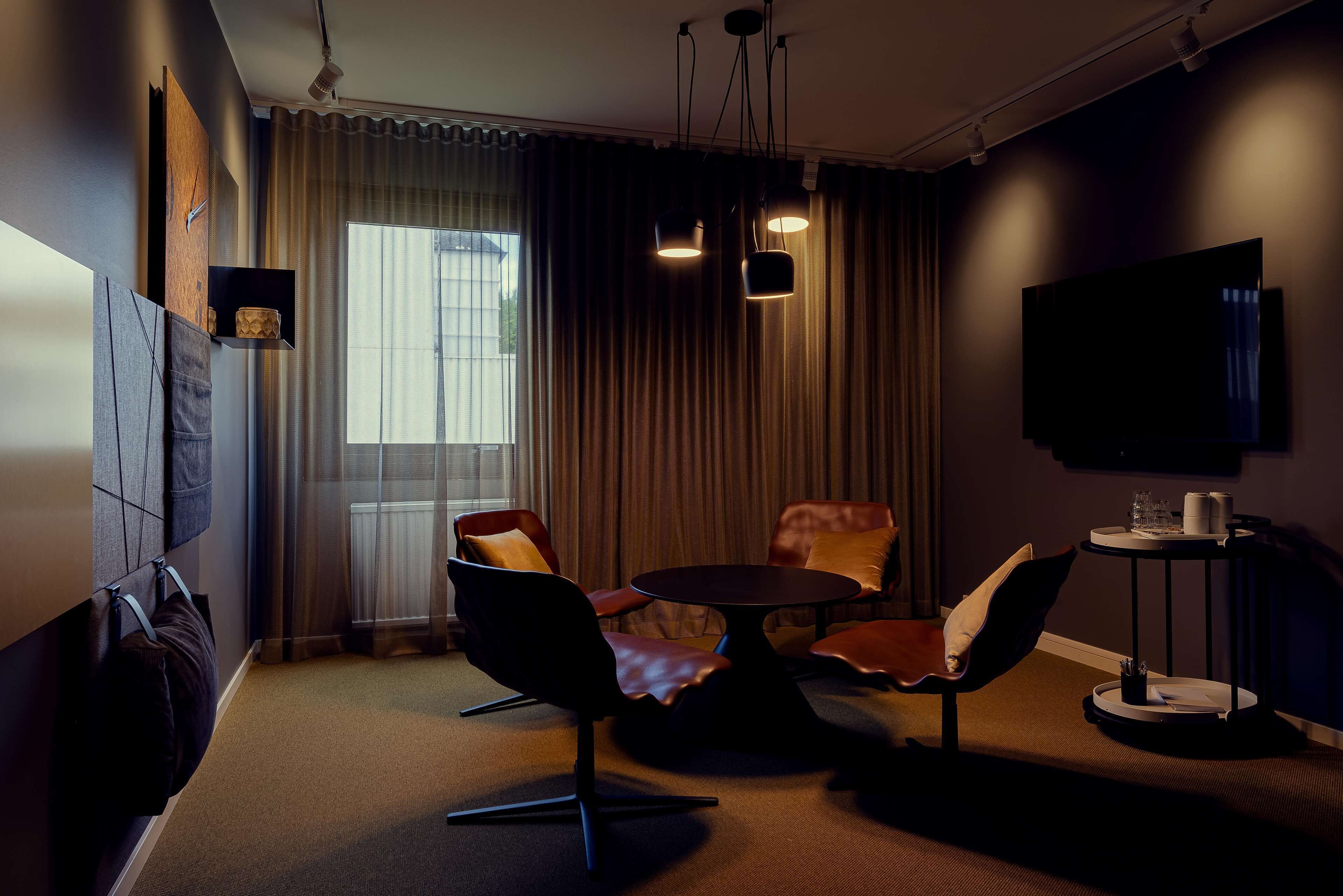 Una habitación de hotel moderna con un ventanal grande, un televisor de pantalla plana y una mesa redonda con sillas.