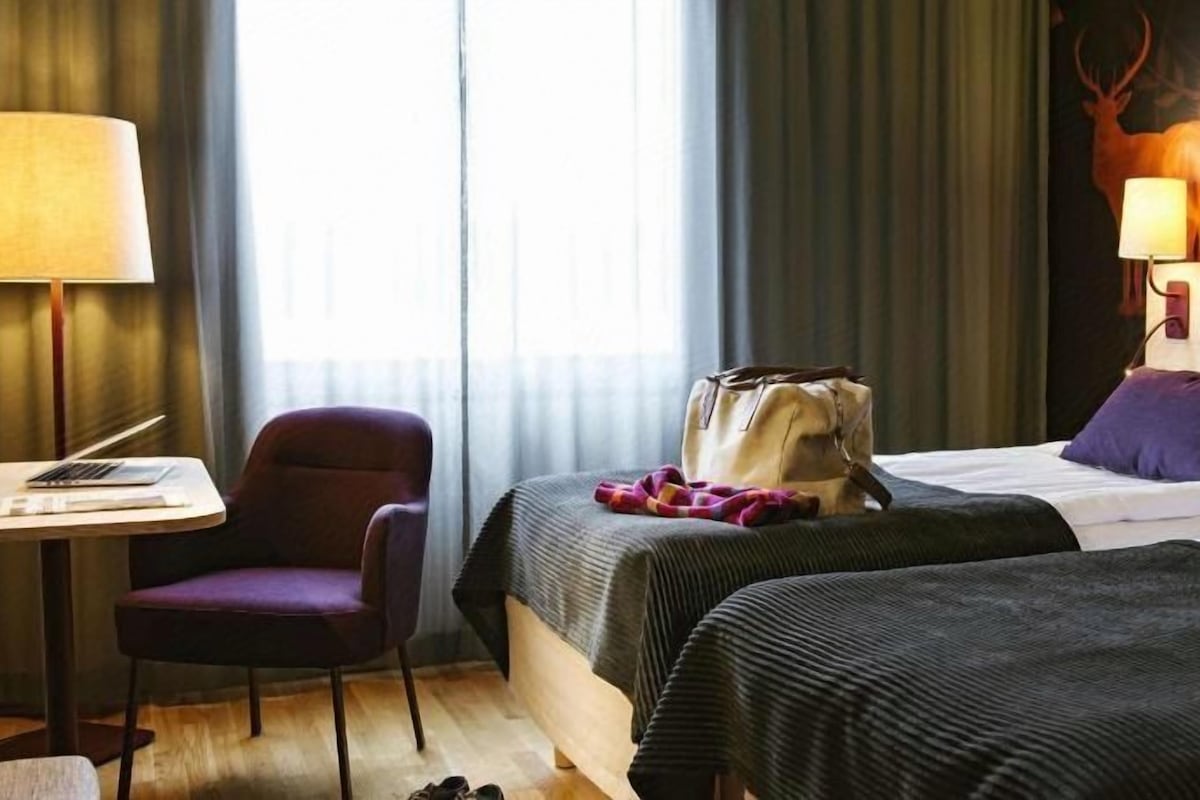 Una habitación de hotel con dos camas, un escritorio, una silla y una lámpara.