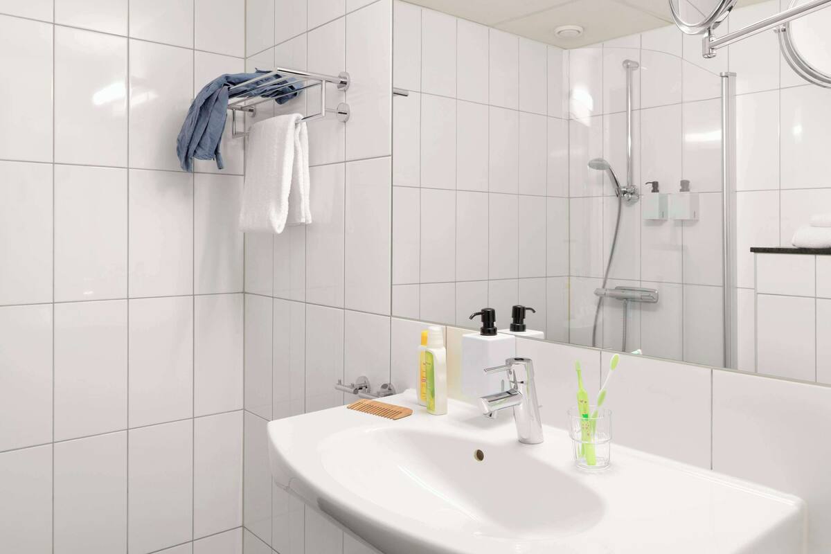 A modern bathroom with a white sink, a mirror, a towel rack, and a shower area.