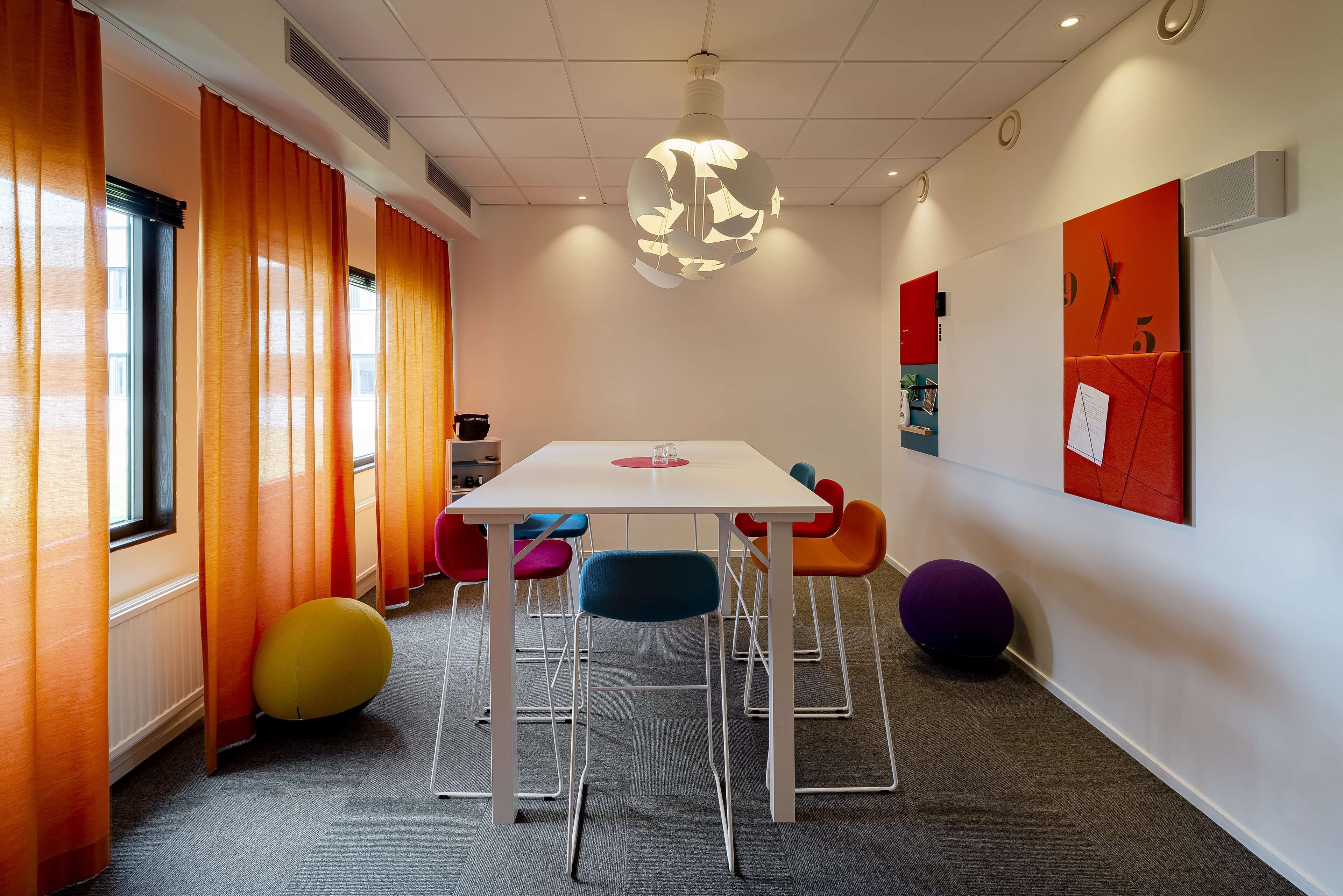 Una sala de reunions moderna amb taula blanca, cadires de colors i una original làmpada esfèrica.