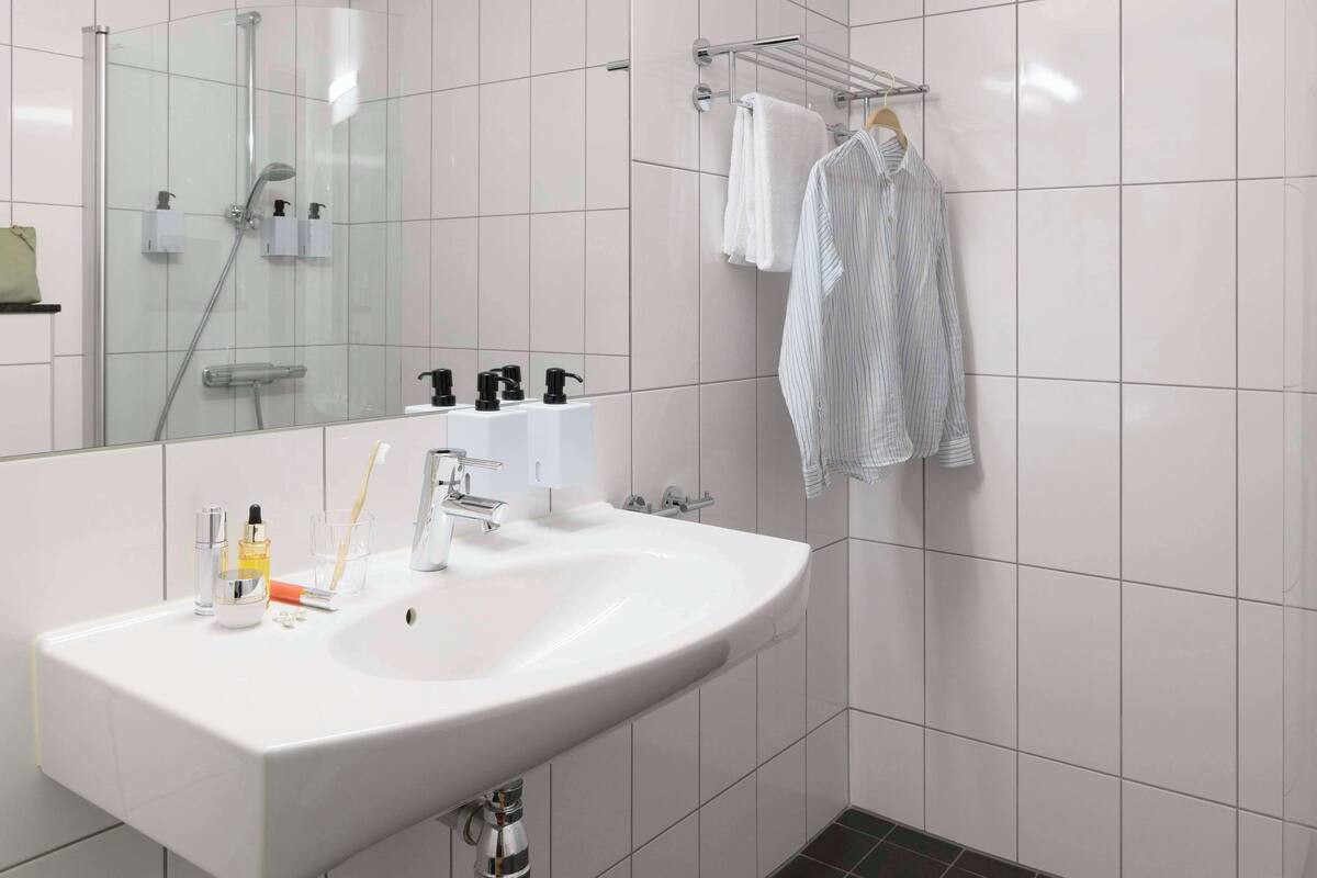 A modern bathroom with a white sink, a glass shower enclosure, and a towel rack with two towels.