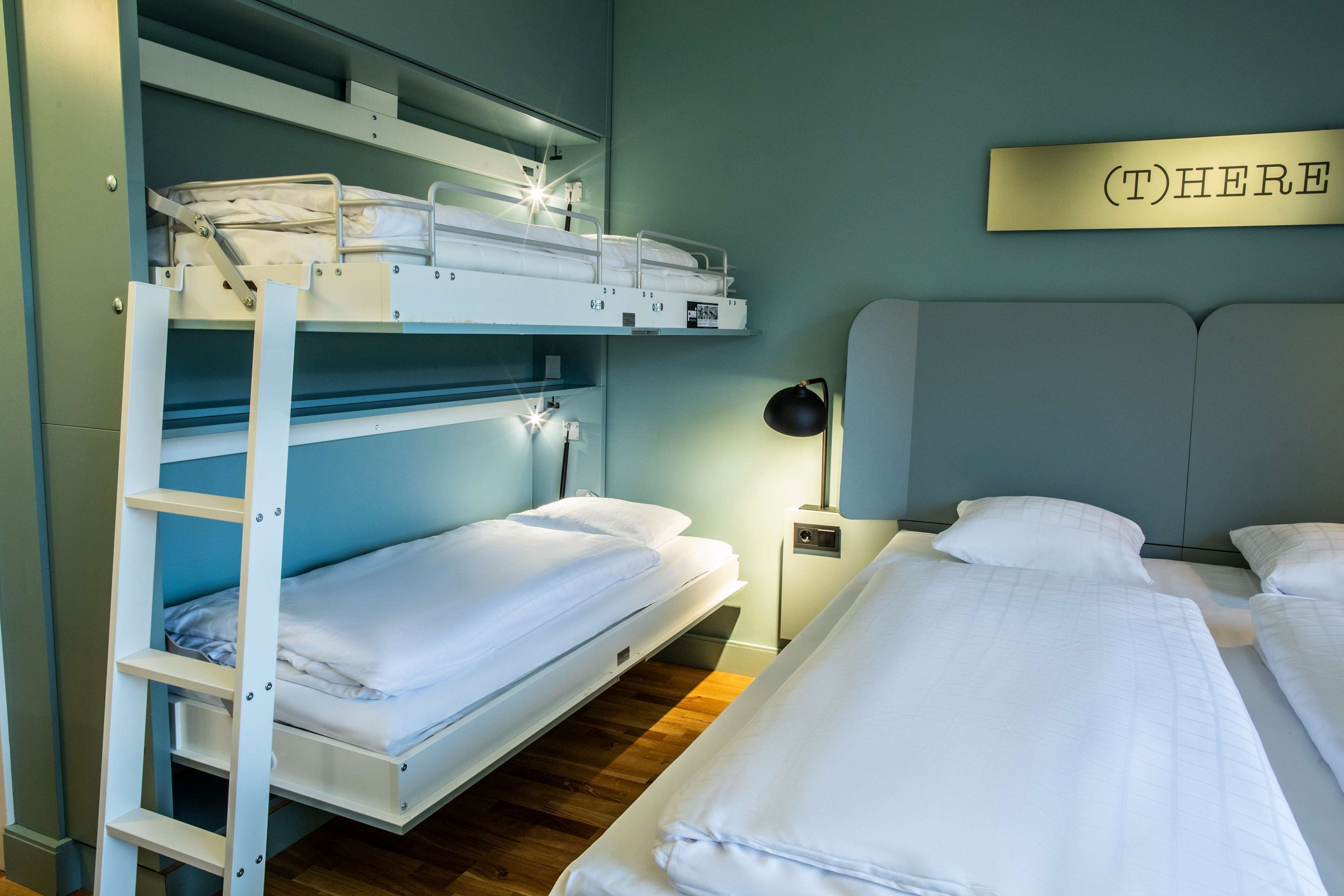 Une chambre avec des lits superposés, sur le mur de laquelle est affiché un panneau indiquant « (I)CI ».