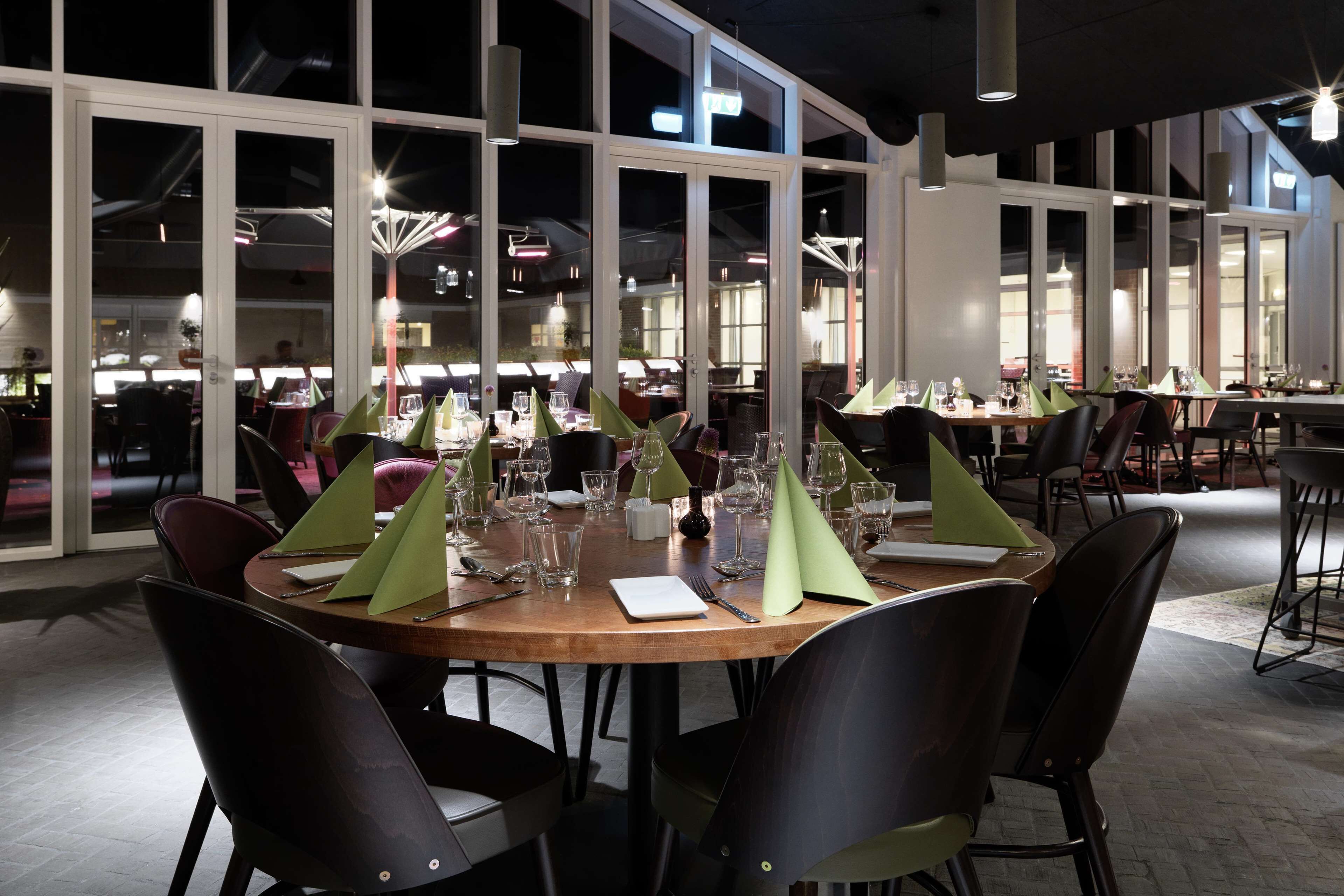 En restaurant med runde borde, store vinduer og moderne indretning.