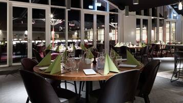 En restaurant med runde borde, store vinduer og moderne indretning.