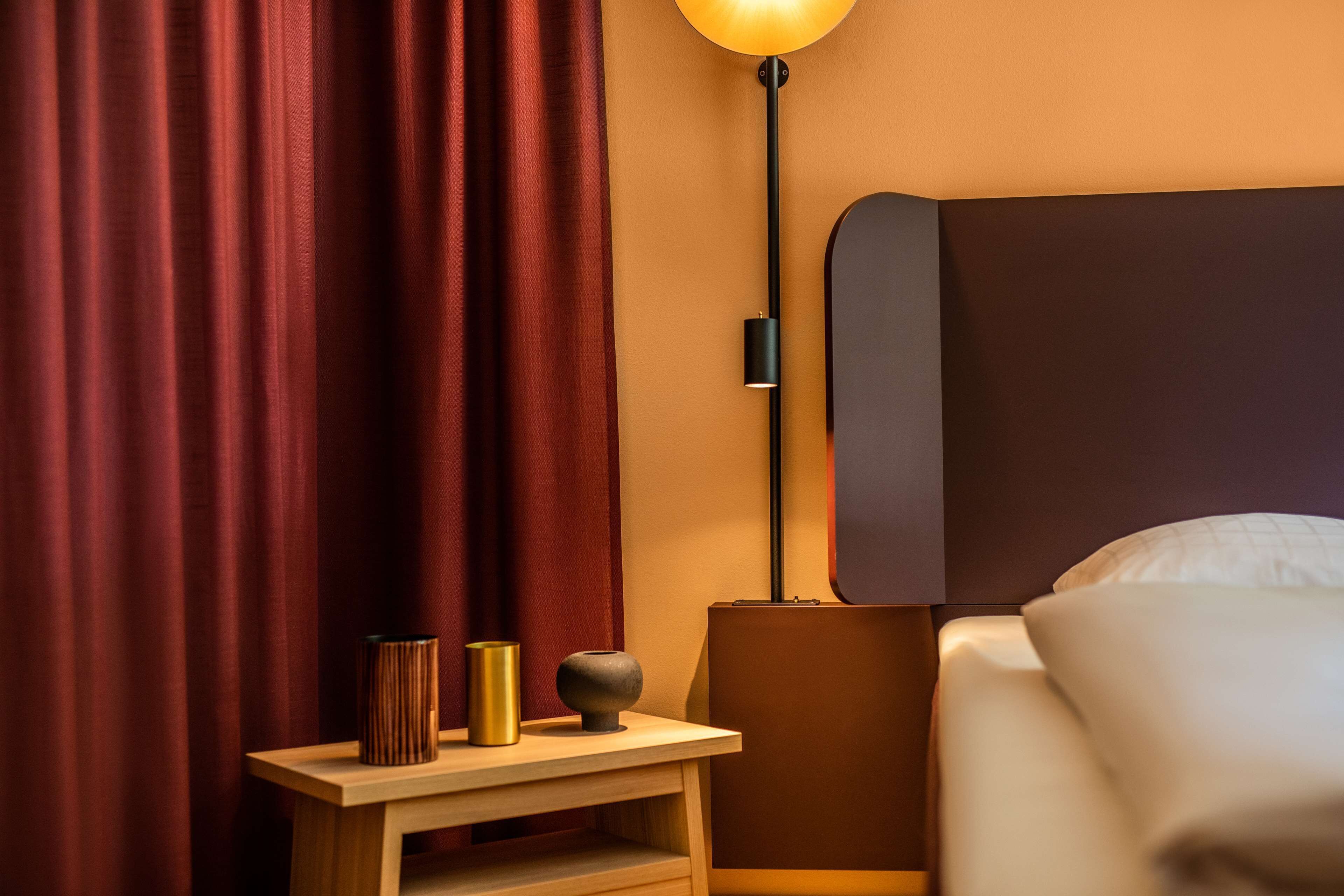 A neatly made bed with white linens, a bedside lamp, and a small wooden nightstand with decorative items.