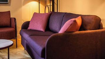 A modern living room with a dark purple sofa, a round wooden coffee table, and a red armchair.