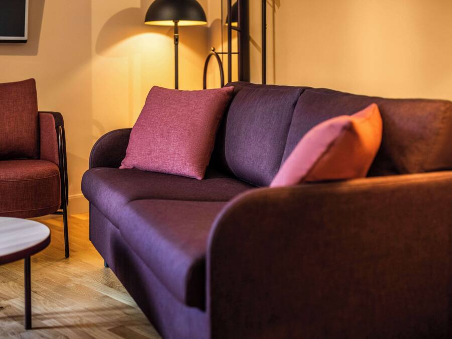 A modern living room with a dark purple sofa, a round wooden coffee table, and a red armchair.