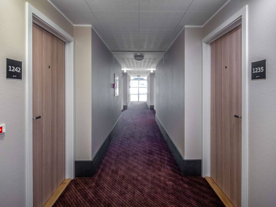 A hallway with carpeted floors, wooden doors, and numbered signs indicating room numbers 1242 and 1235.