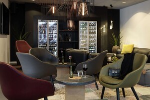 Un espacio lounge moderno con sofás de cuero, una mesa redonda con un florero y una copa de vino, y un aparador para zapatos.