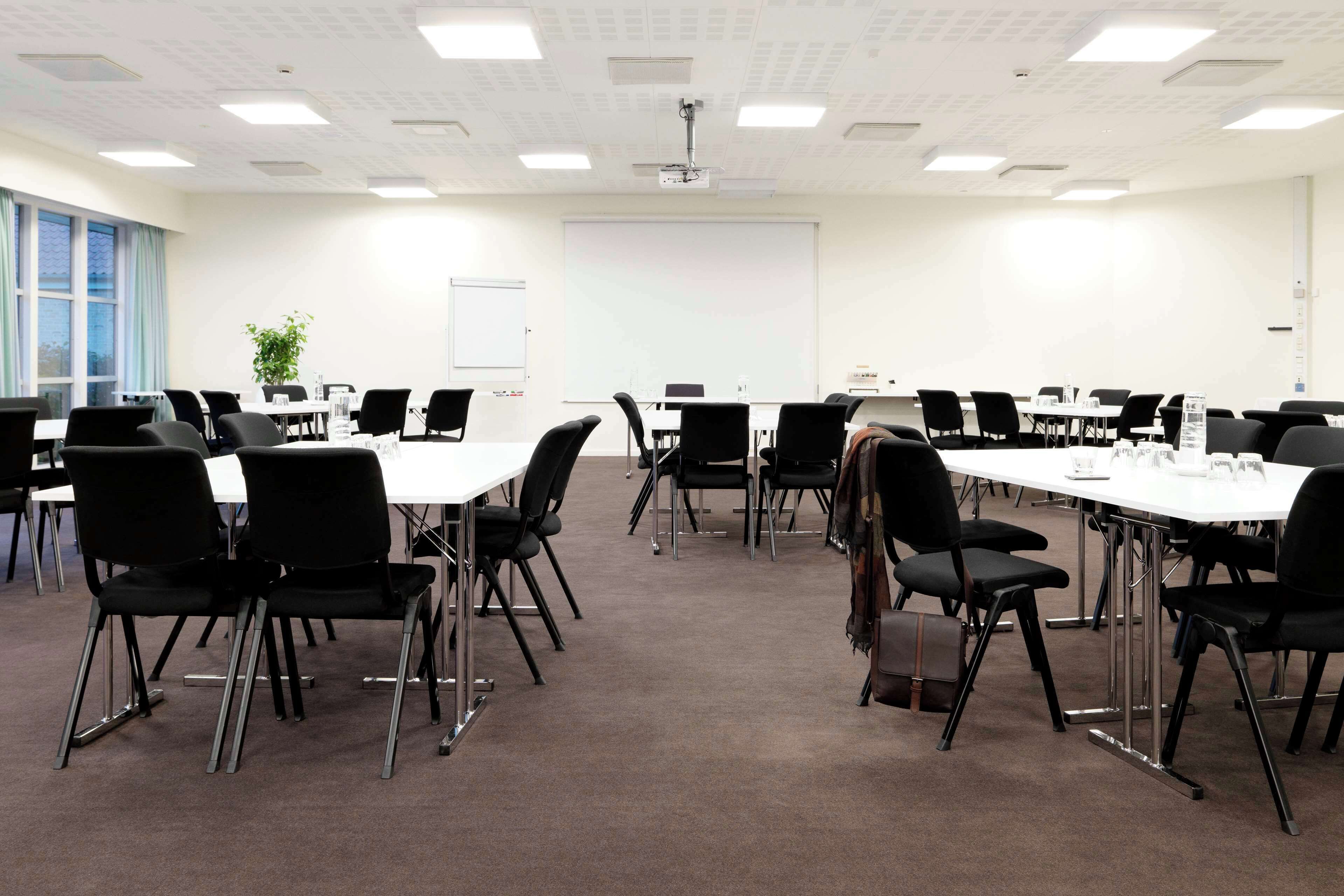 Un salón de conferencias con varias mesas y sillas, una pizarra y una pantalla para proyector.