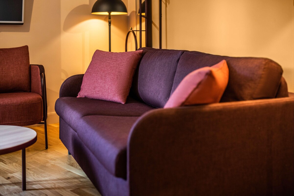 A modern living room with a purple sofa, a round coffee table, and a floor lamp.