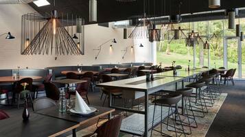 Un restaurante moderno con mesas comunitarias largas, asientos individuales y lámparas colgantes.