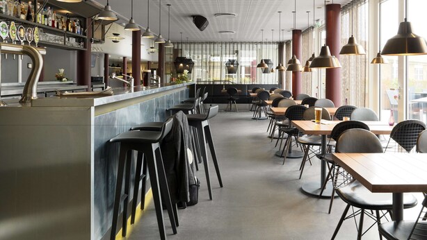 Una zona de bar moderna amb una barra llarga, diverses banquetes i lluminàries penjants.
