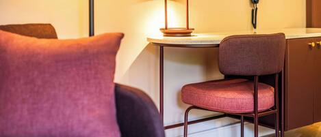 Una habitación moderna con un sofá de color oscuro, un sillón rojo acolchado, una pequeña mesa redonda con una lámpara y un teléfono en la pared.