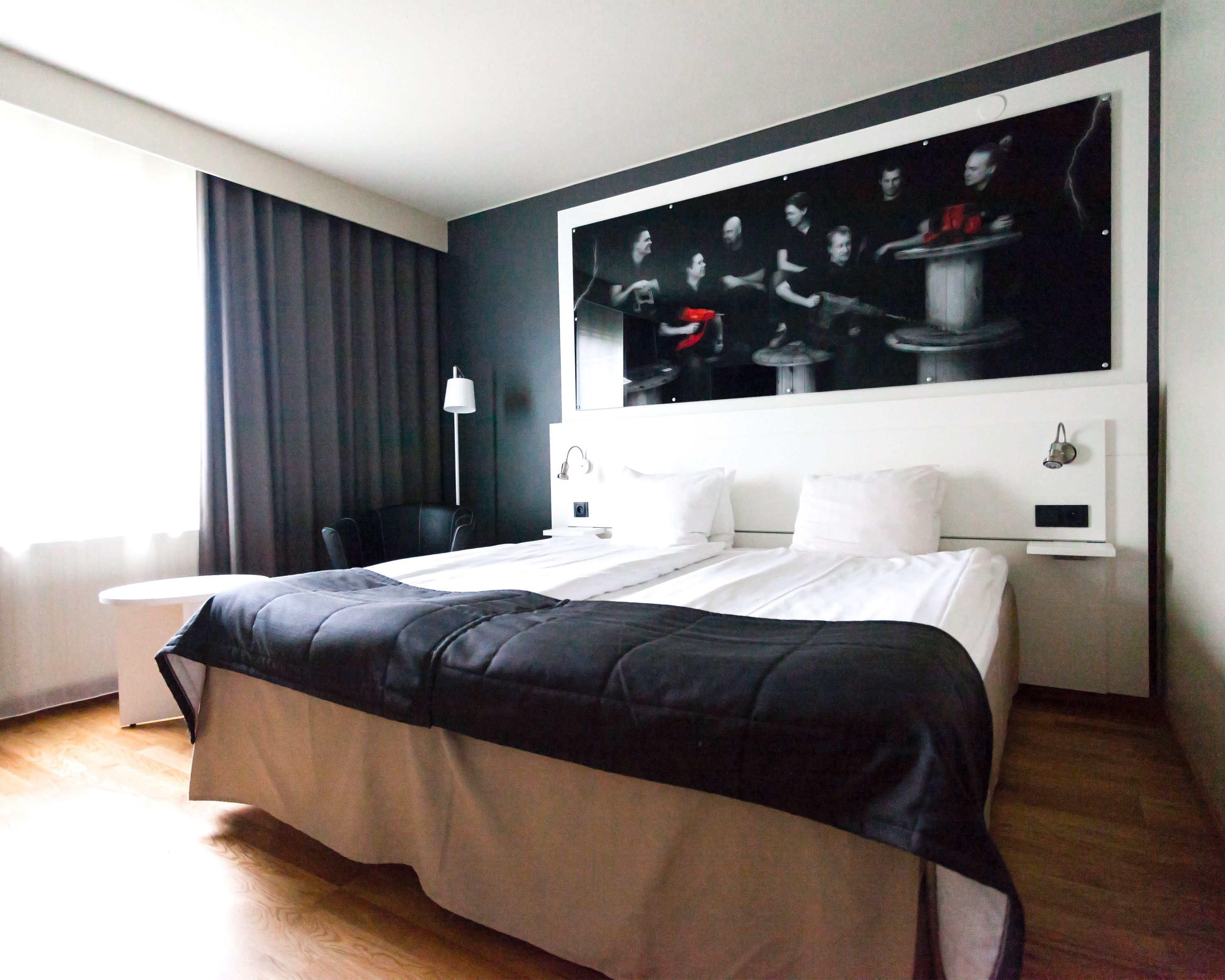 A modern hotel room with a large bed, a desk, and a painting on the wall.