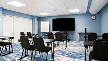 Un salón de conferencias con una pantalla grande, mesas y sillas dispuestas para reuniones.