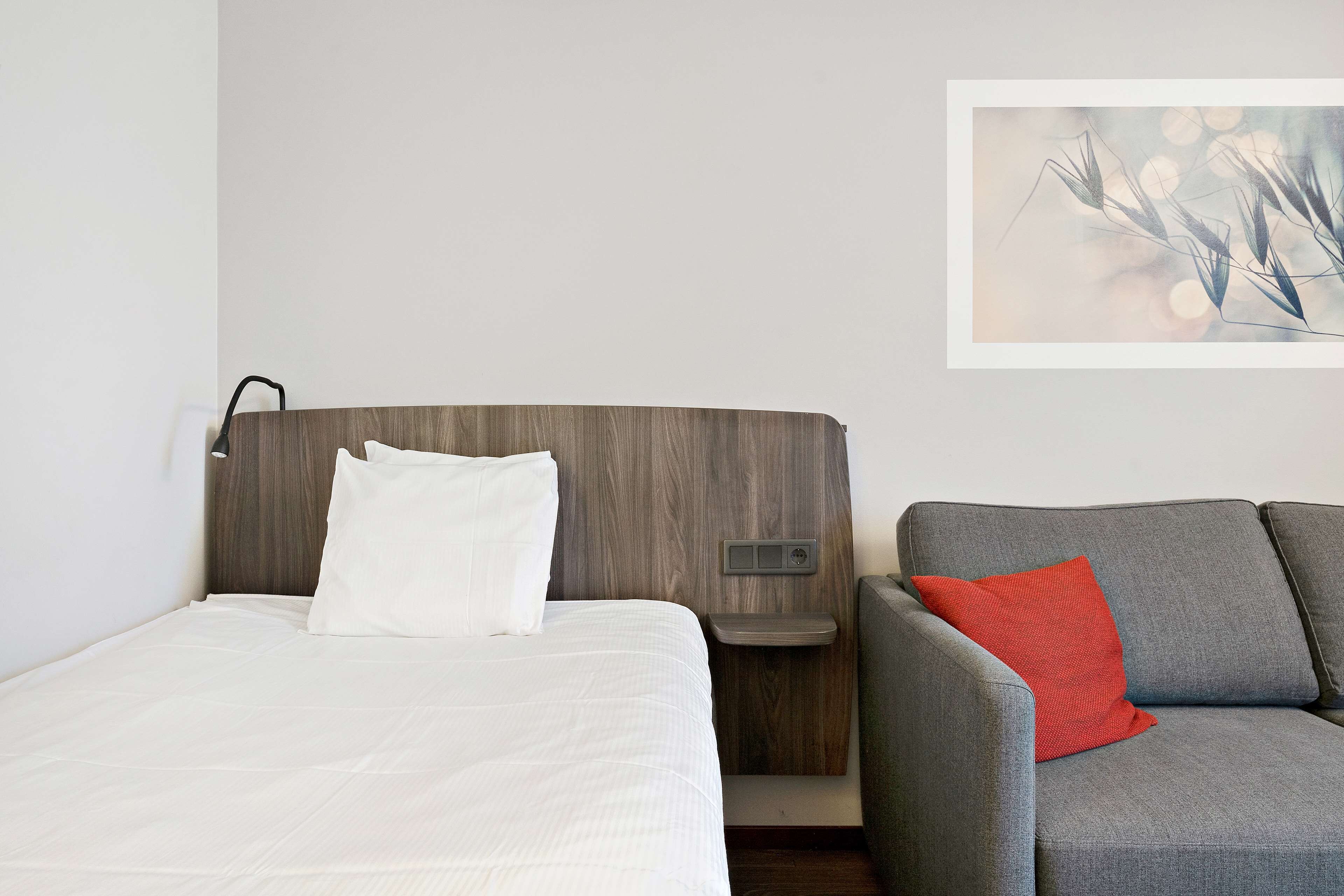 A hotel room with a bed, a gray sofa, and a wall-mounted control panel.