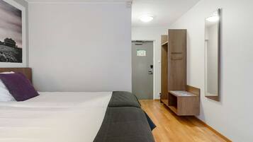 A hotel room with a bed, a wooden bench, a mirror, and a door leading to a bathroom.