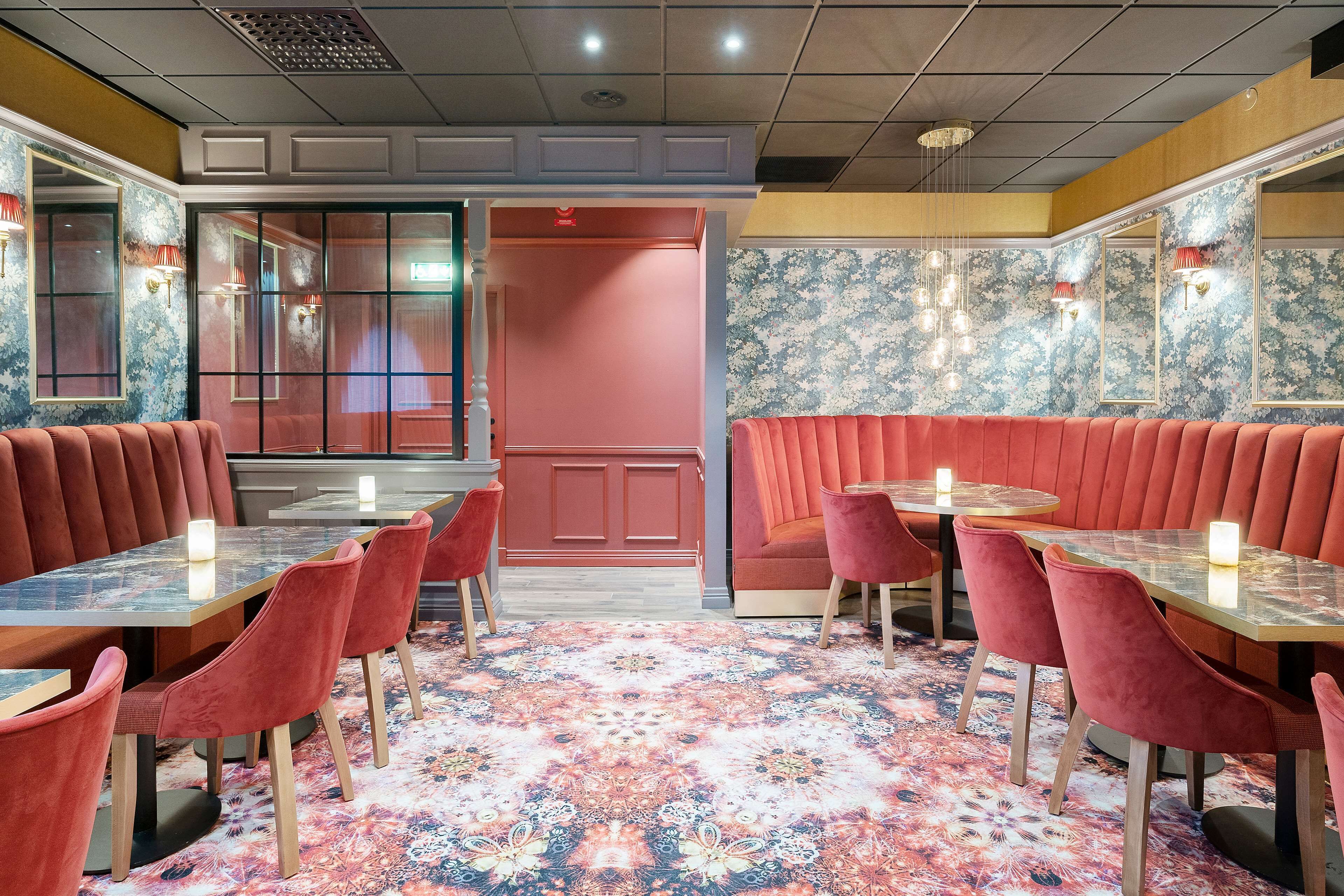 A restaurant with booths and tables, a patterned carpet, and wall sconces.