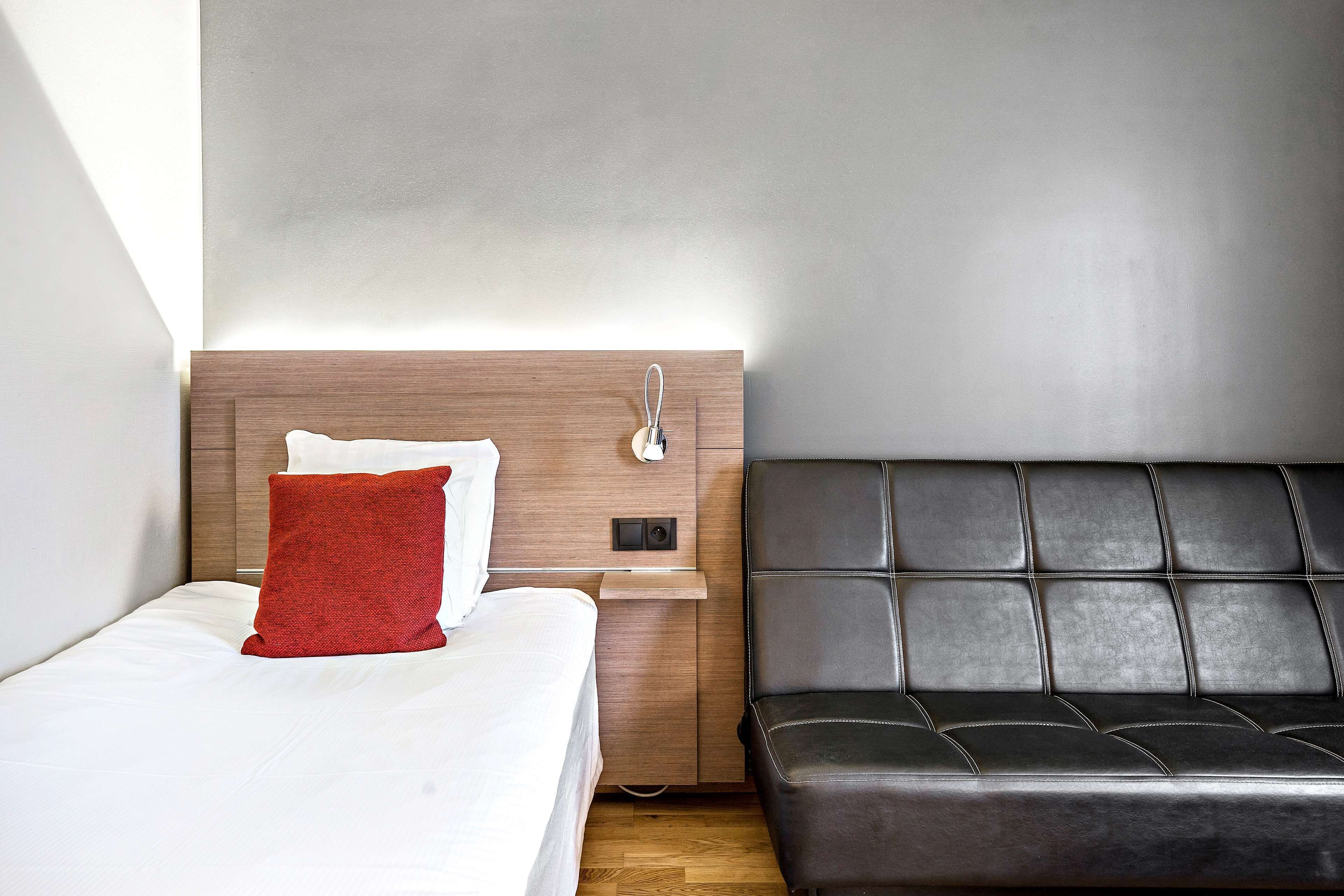 Quarto de hotel com cama, mesa de cabeceira e sofá de couro.
