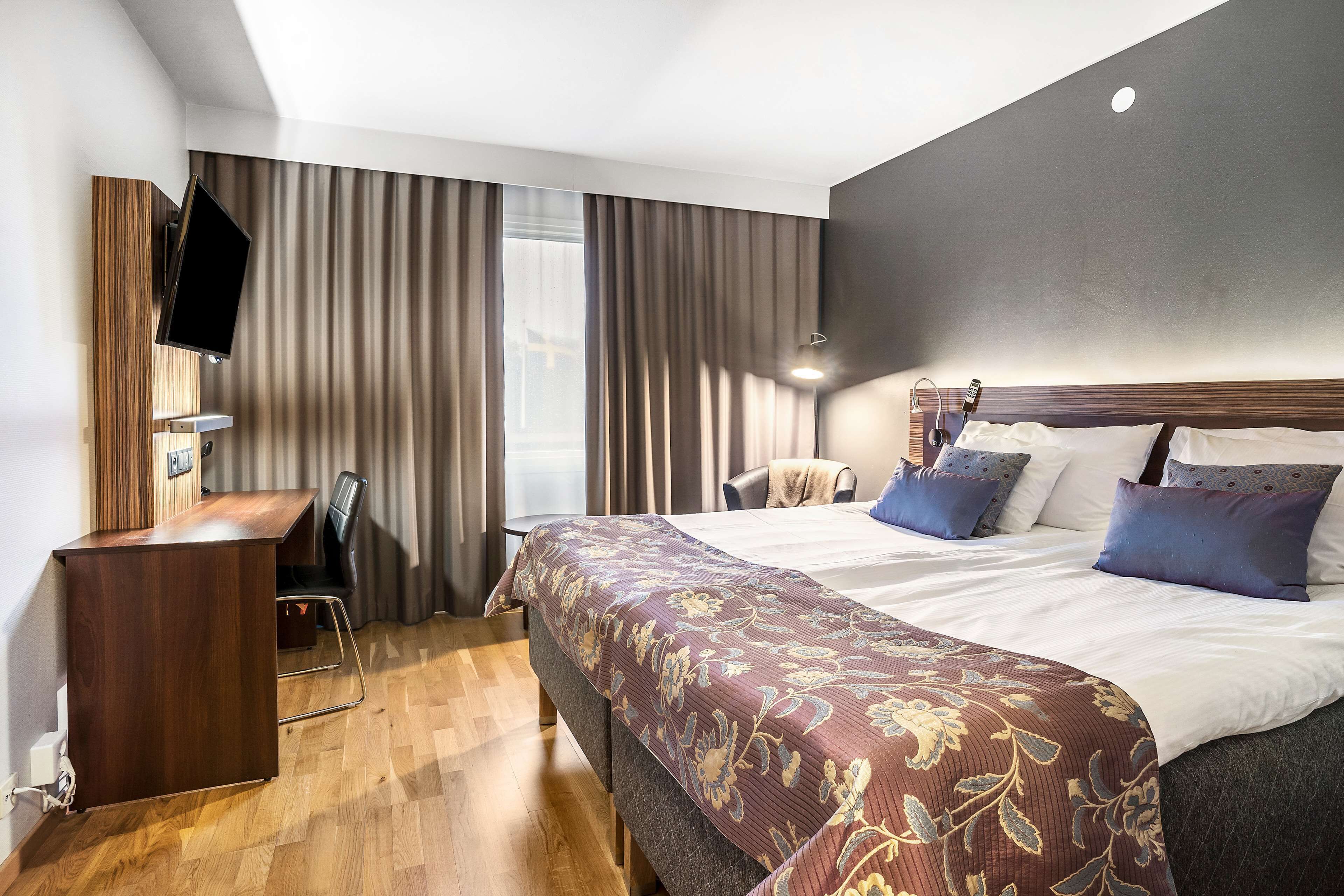 Een hotelkamer met een groot bed, een bureau, een stoel en een aan de muur bevestigde televisie.