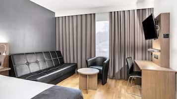 A modern hotel room with a leather sofa, a small round table, a desk with a chair, and a TV mounted on the wall.