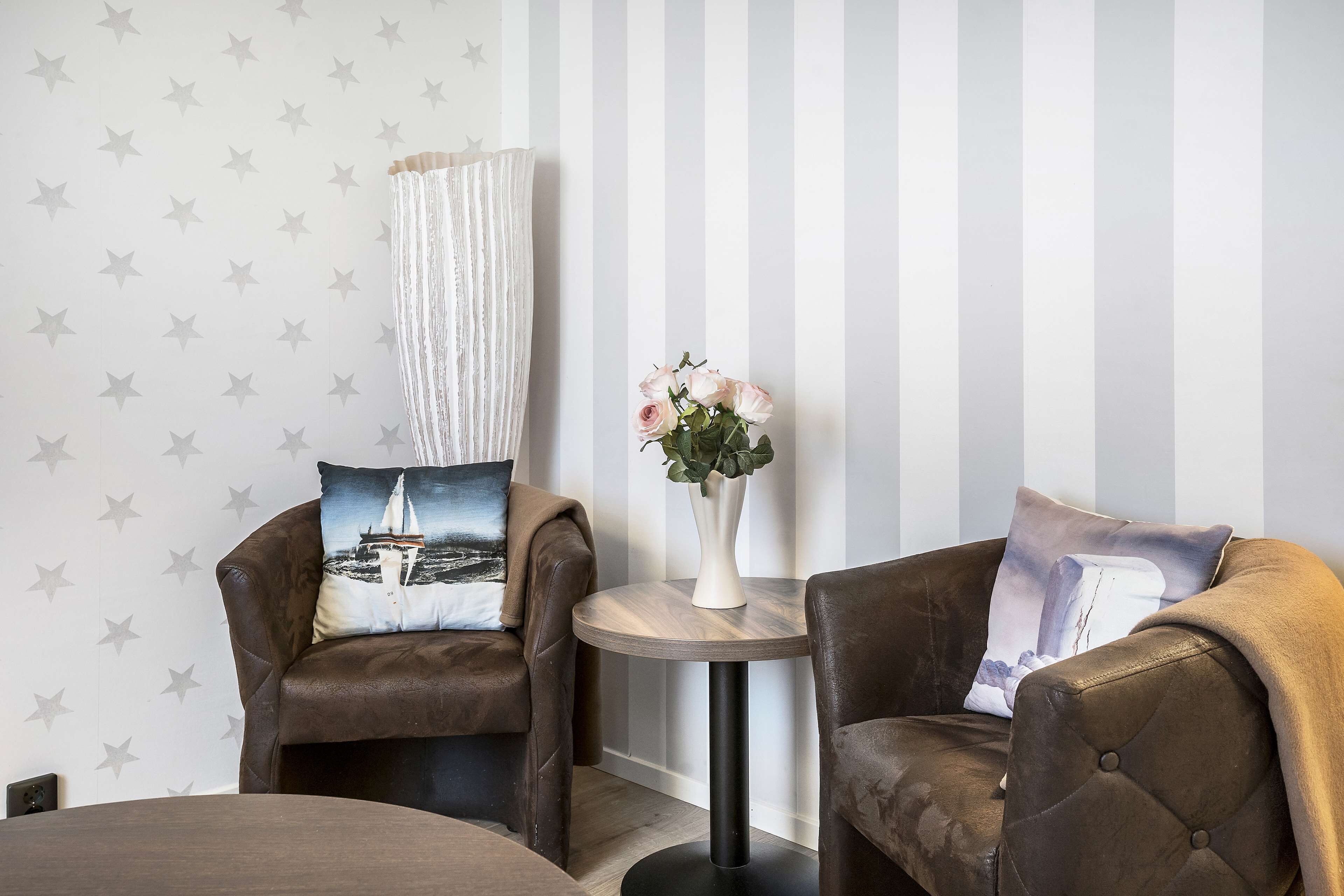 A room with two brown leather armchairs, a round wooden side table with a vase of flowers, and a striped wall with star patterns.