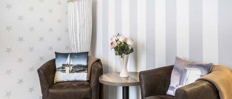 A room with two brown leather armchairs, a round wooden side table with a vase of flowers, and a striped wall with star patterns.