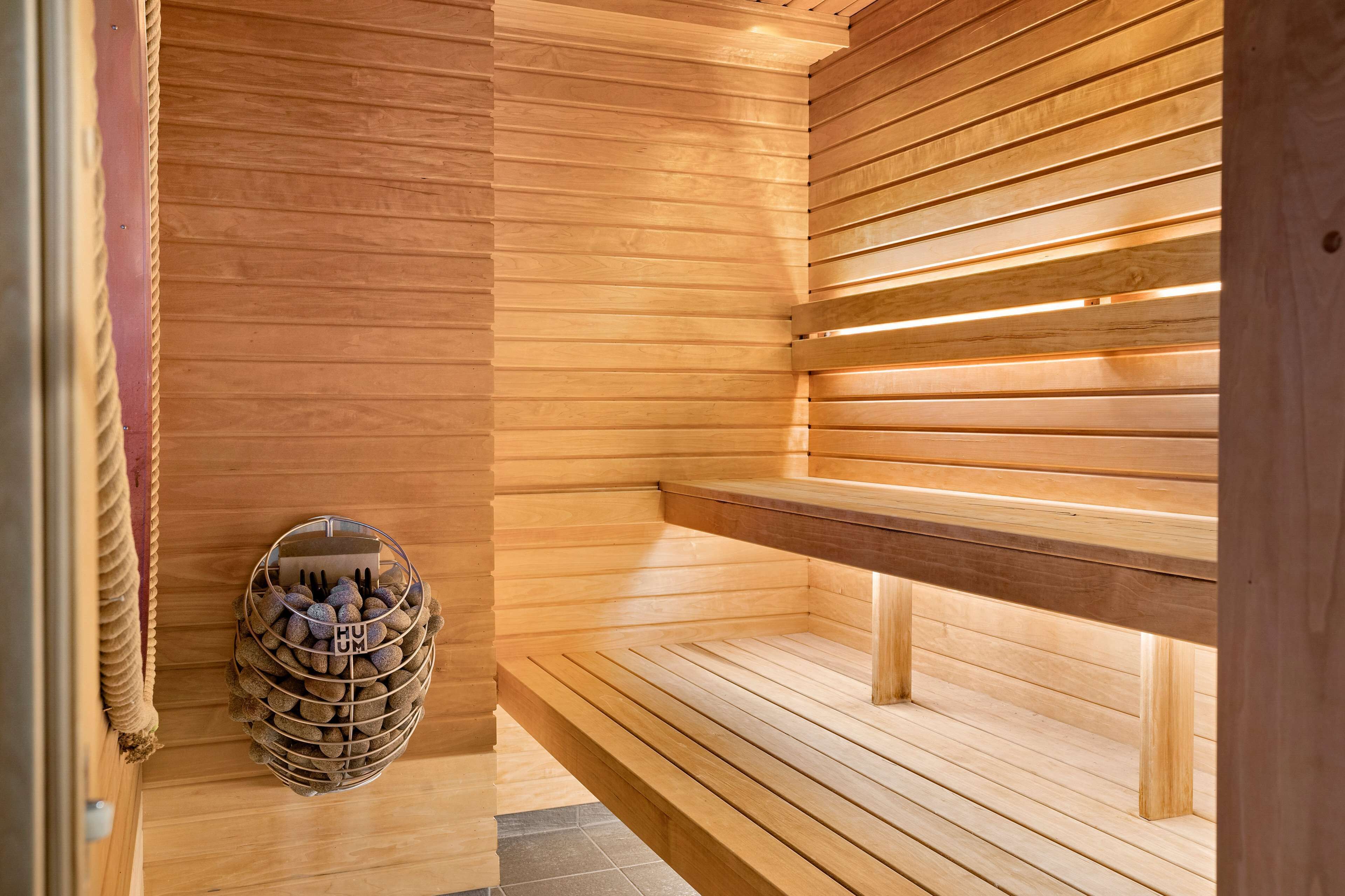 A sauna with wooden benches and a metal basket of stones.