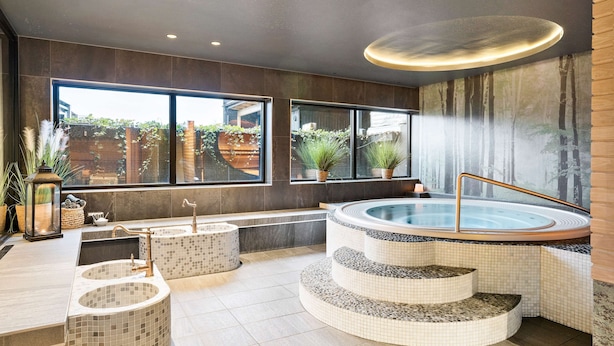 Un área de spa con jacuzzi, escalones revestidos con mosaicos y ventanas amplias que ofrecen vistas al exterior.