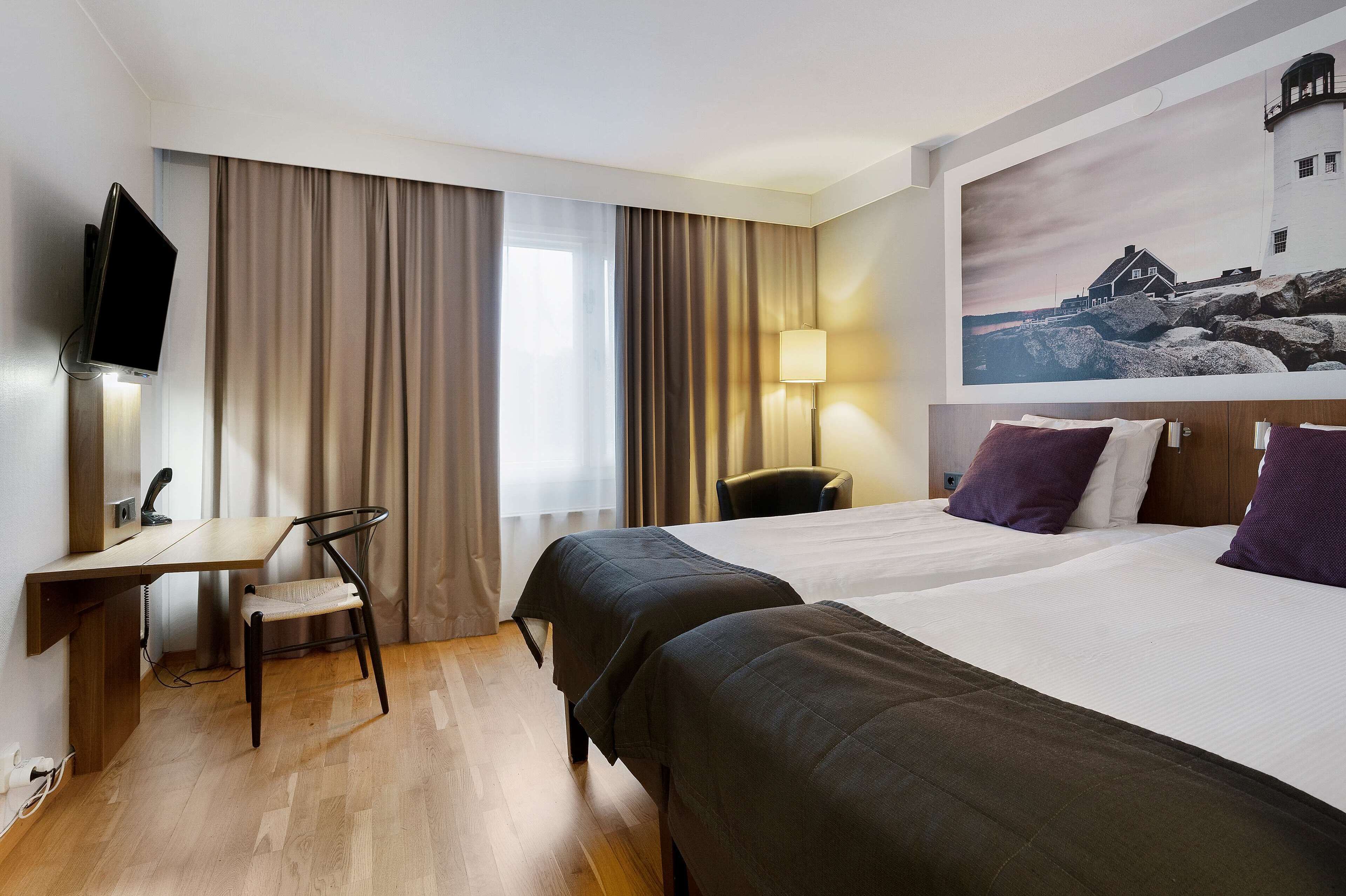 Habitación de hotel con dos camas, un escritorio, una silla, un televisor y un cuadro en la pared.