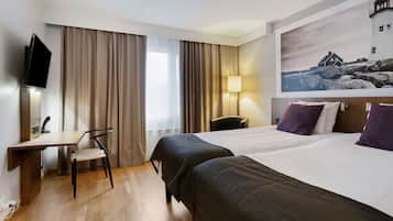 Habitación de hotel con dos camas, un escritorio, una silla, un televisor y un cuadro en la pared.