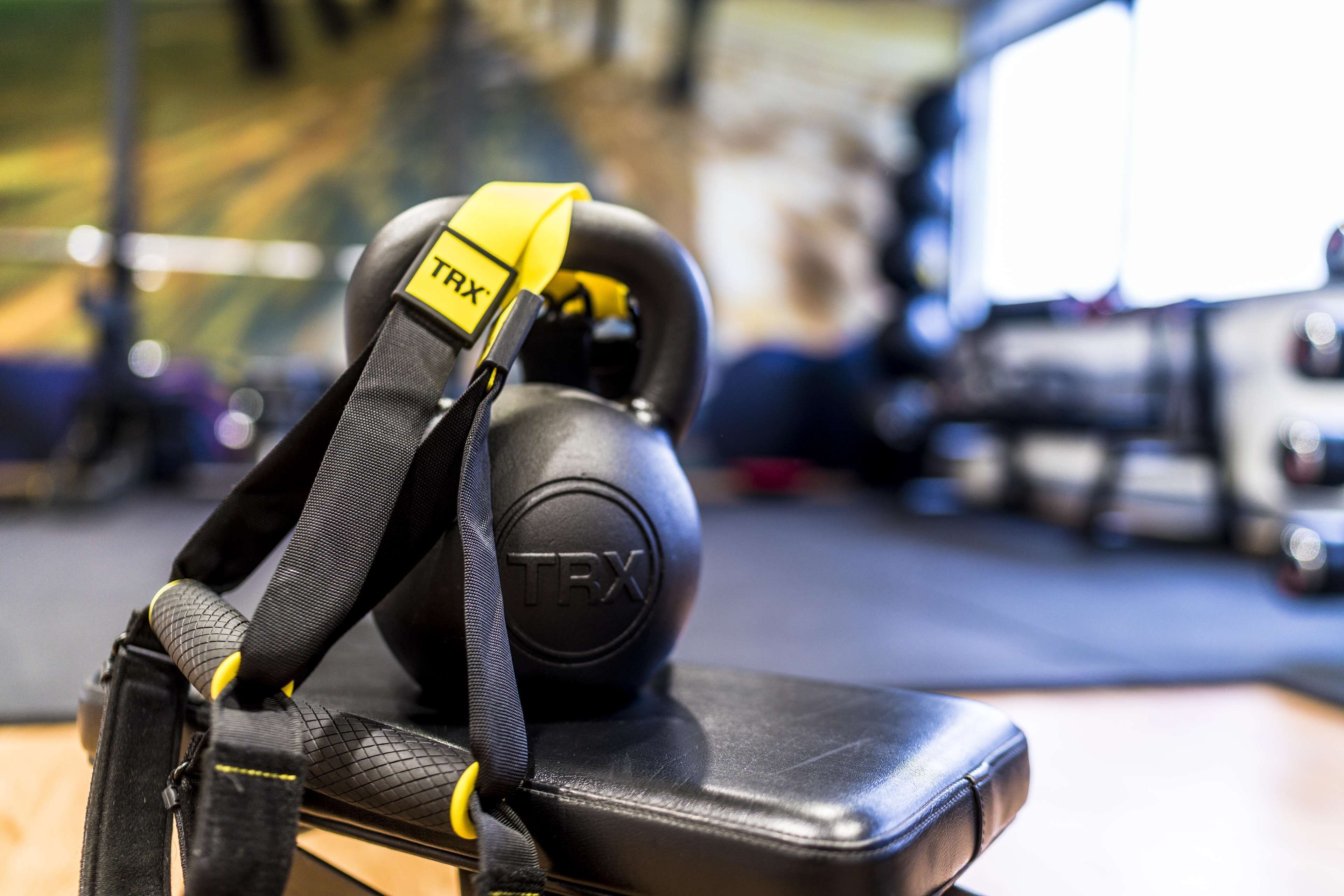 A TRX suspension trainer with a black handle and yellow accents, placed on a black leather bench in a gym.