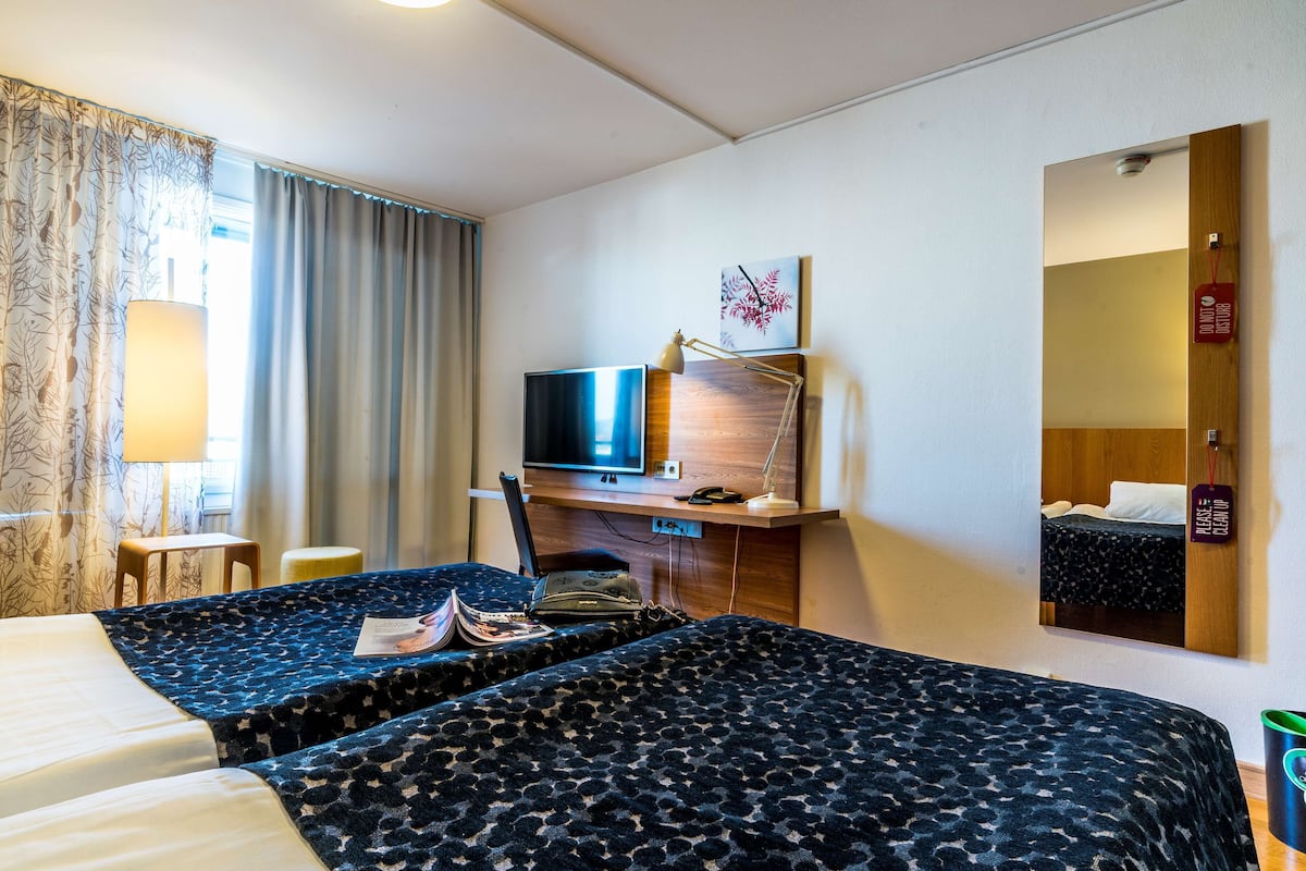 A hotel room with two beds, a desk with a computer, a TV, and a large mirror.