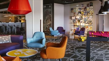 A modern lounge area with bar seating, a pool table, and a wall decorated with magazines and posters.