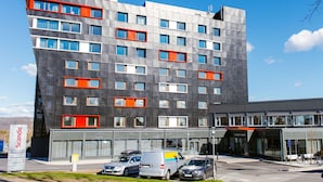 Edifici d'hotel modern amb un rètol prominent de 'Scandic', diversos pisos i una zona d'aparcament amb diversos cotxes.