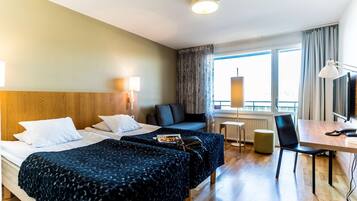 Habitación de hotel con dos camas, un escritorio, una silla, un televisor y una ventana con cortinas.