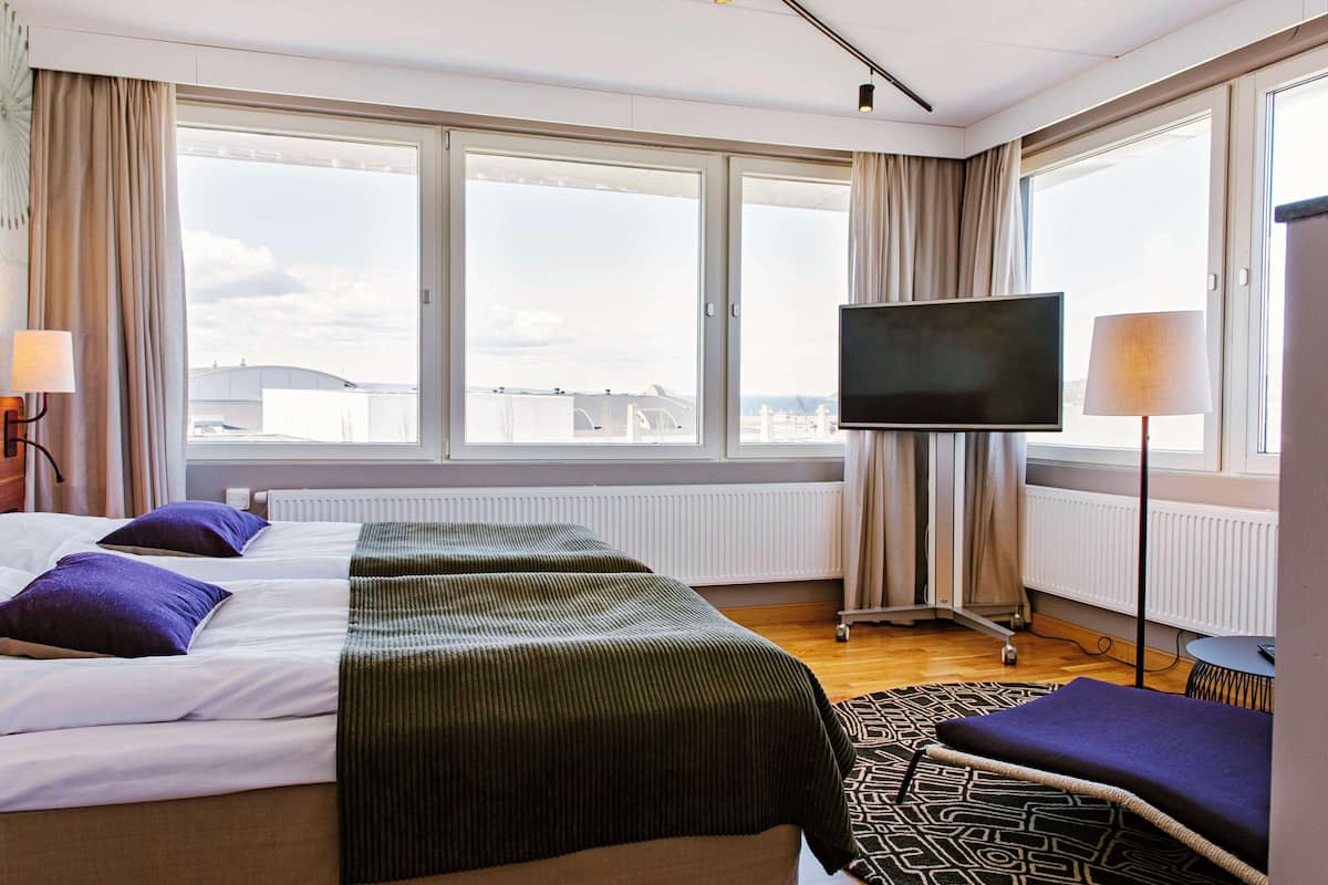 A hotel room with a large bed, two pillows, a TV, and a view of the city.