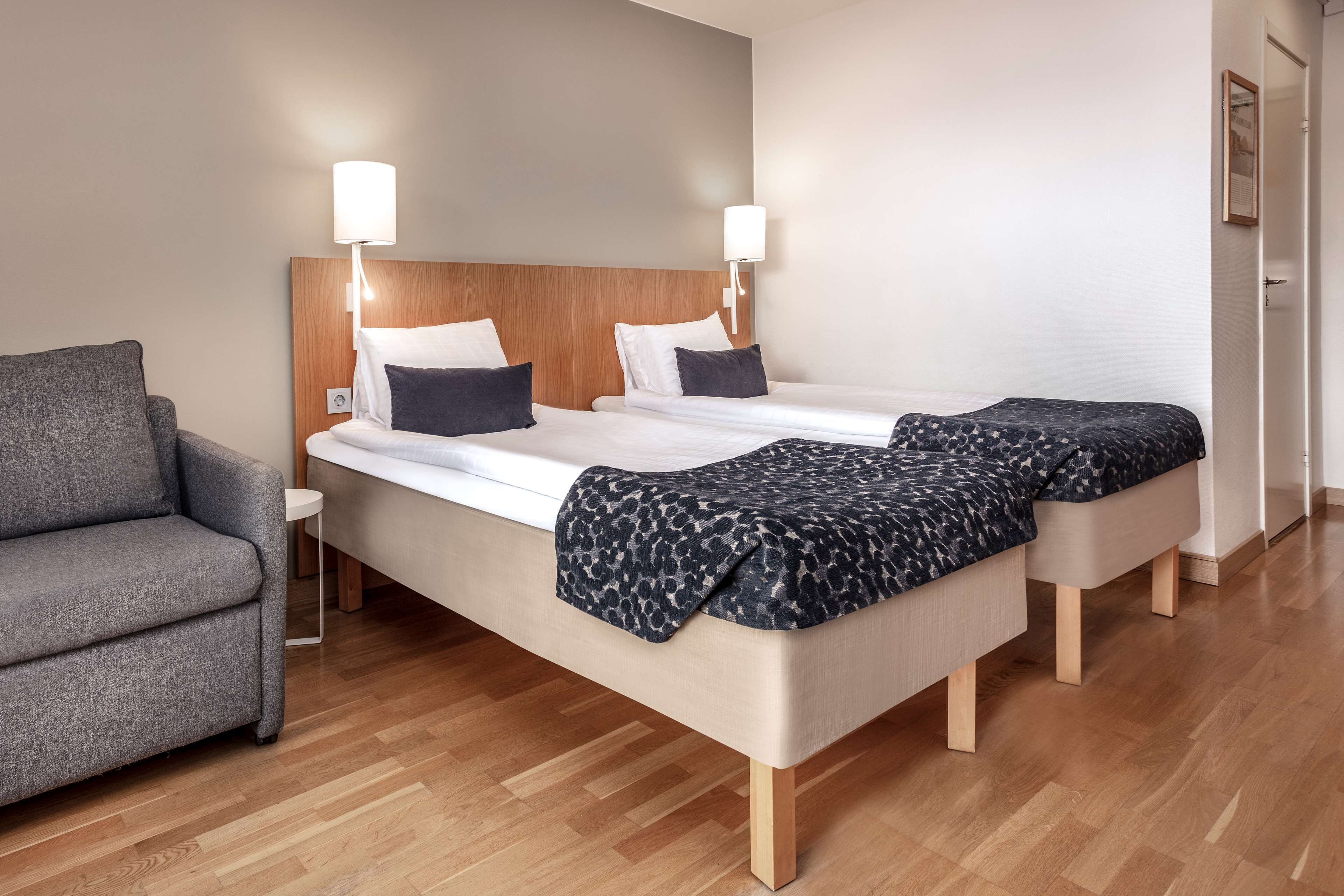 Ein Hotelzimmer mit einem Bett, zwei Nachttischen, einem grauen Sessel und Holzboden.